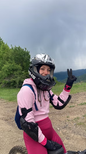 Adriana Milcheva in riding gear on a dirt trail, with green hills behind her.
